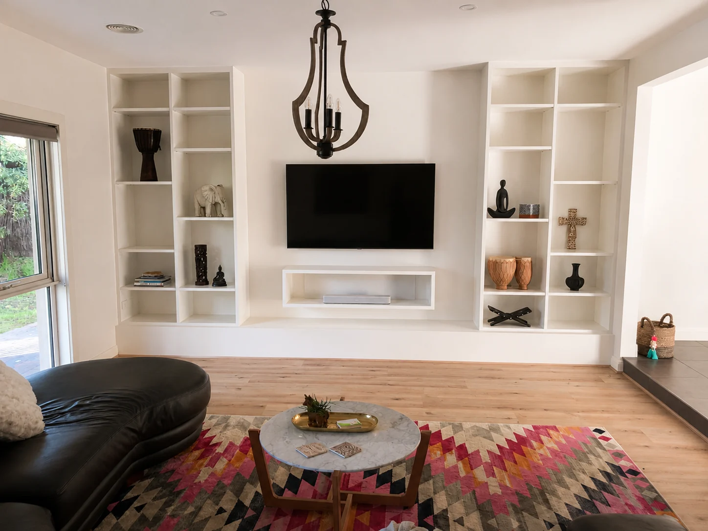 Contemporary living room showcasing one of the top modern built in tv wall unit designs with a marble accent backdrop, hidden storage cabinets, and open display shelves.